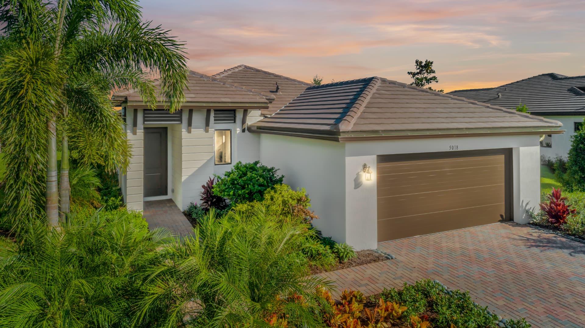 Florida home exterior at dusk with landscaped palm trees and paver driveway